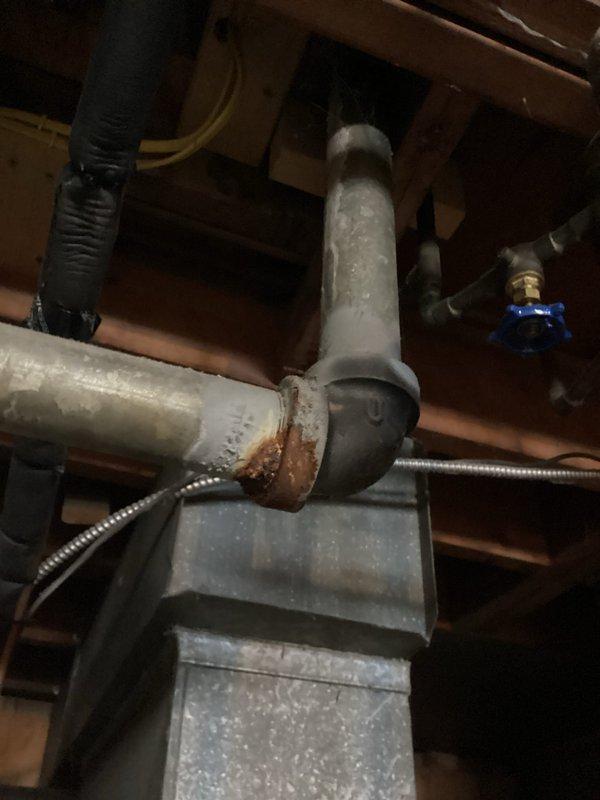 Conducted comprehensive plumbing inspection of basement utility area, focusing on HVAC equipment and water heater installation. Identified significant rust and corrosion at pipe elbow joint where horizontal metal pipe connects to vertical pipe, with potential moisture issues that require attention.