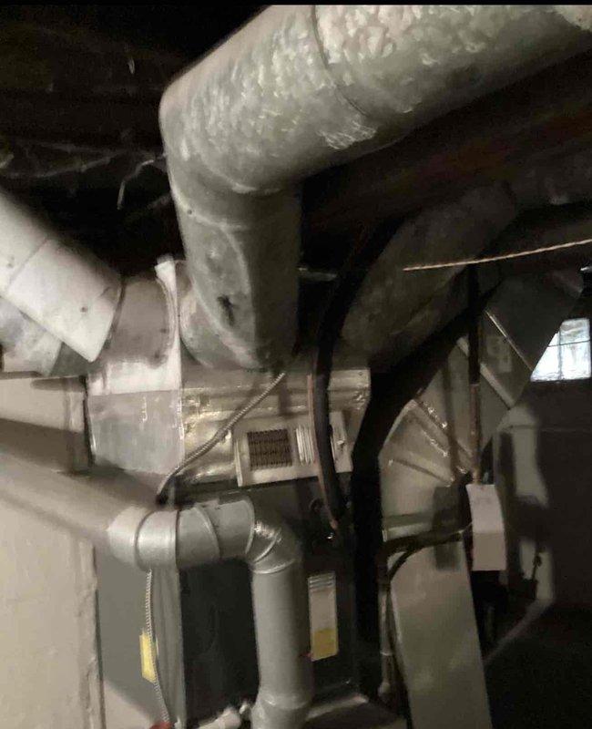 Completed inspection of aging furnace system in basement utility area. Examined existing Rheem unit with PVC ventilation pipes, noting worn components and connection points. Provided replacement options for the older HVAC system, documenting current installation configuration including ductwork condition and ventilation requirements.