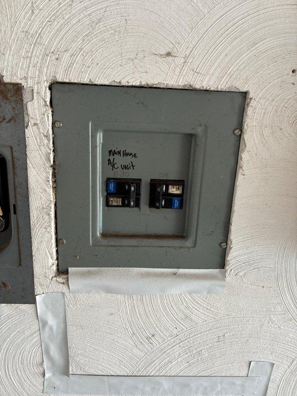 Conducted inspection and prepared estimate for replacement of existing HVAC unit located in utility closet with wooden enclosure. System includes black insulated refrigerant lines, PVC drainage, and copper tubing connections. Also evaluated electrical sub-panel labeled "MAIN HOUSE A/C UNIT" showing signs of aging with potential upgrade requirements to support new system installation.