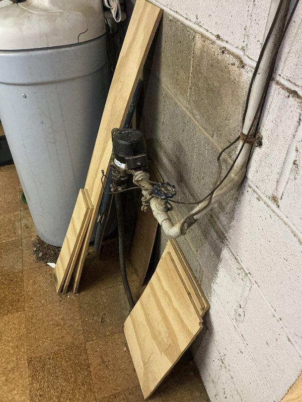 Performed electrical inspection of service panel in basement area. Inspected circuit breaker panel mounted on concrete block wall, examining wiring connections and breaker functionality. Also observed water pump/valve assembly with PVC piping connections adjacent to utility tank.