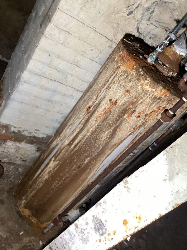 Conducted inspection of water heater system exhibiting severe corrosion. Unit shows extensive rust formation throughout the tank body with significant deterioration at connection points and top surface. Observed water/moisture intrusion at pipe connections and rust streaks extending down tank sides, indicating ongoing water issues accelerating the corrosion process.