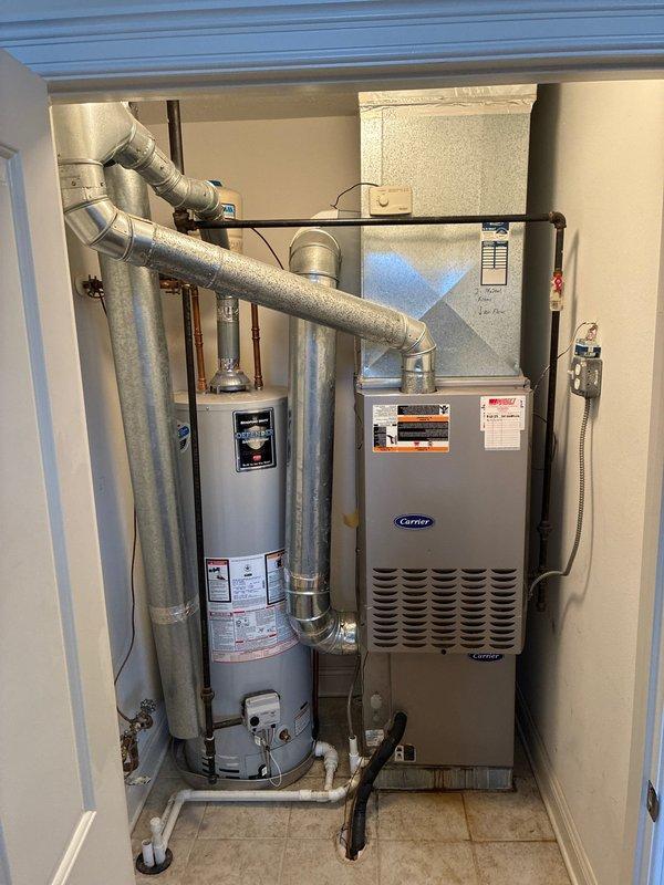 Conducted full system evaluation of existing Carrier HVAC equipment in utility closet. Inspected furnace with front panel open to assess internal components including control board, wiring and mechanical elements. Documented condition of ductwork, connections, and adjacent water heater to prepare comprehensive system replacement options for client consideration.
