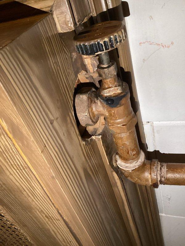 Conducted comprehensive inspection of radiator system throughout residence, focusing on aged copper plumbing components and valve assemblies showing signs of oxidation and potential leakage. Identified brass valve with black ribbed hand wheel requiring attention due to visible corrosion at connection points, with particular concern noted at the threaded junctions where white tape/sealant was previously applied.