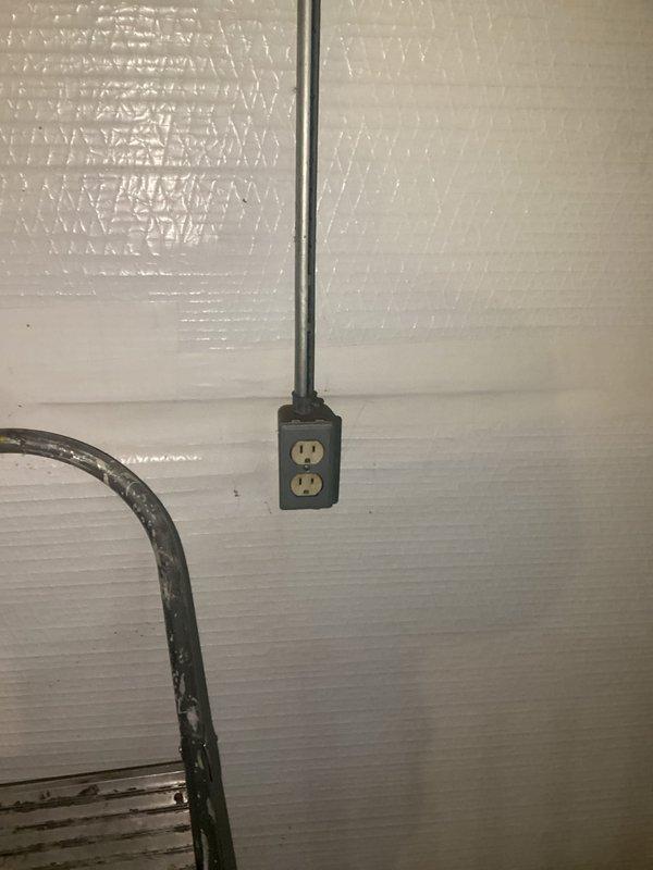 Conducted mid-morning electrical inspection of wall-mounted outlet with metal conduit extension and documented condition of surrounding reflective paneled wall. Examined electrical cord installation on concrete/tile floor, noting presence of connector/adapter with attached tag and proximity to metal wire structure.
