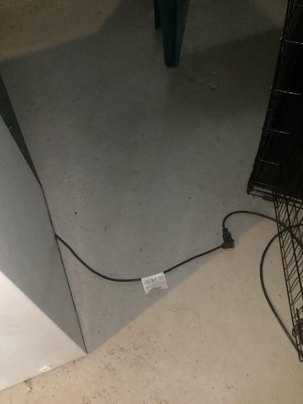 Conducted mid-morning electrical inspection of wall-mounted outlet with metal conduit extension and documented condition of surrounding reflective paneled wall. Examined electrical cord installation on concrete/tile floor, noting presence of connector/adapter with attached tag and proximity to metal wire structure.