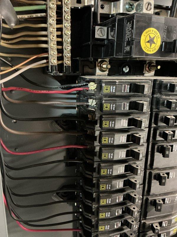 Conducted electrical inspection of circuit breaker panel, confirming proper installation of Square D breakers with no visible damage or abnormal wear. Examined wall-mounted electrical outlet with indicator light and inspected surrounding structural elements including wooden support beams and ceiling components.