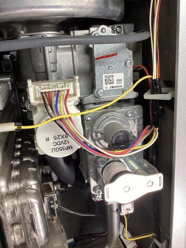 Diagnosed loud grinding noise in Rinnai tankless water heater during operation. Inspection revealed faulty flow control motor (MP36GU 12VDC) with worn components. Replaced flow control motor assembly and verified proper operation with no further noise during heating cycles.