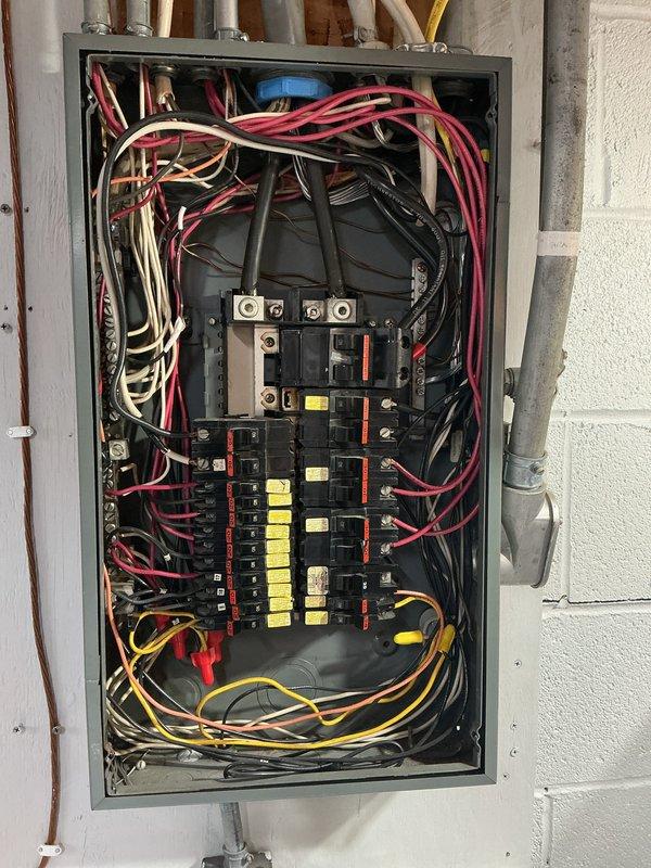Performed comprehensive electrical panel inspection, documenting circuit breaker configuration and wiring condition. Noted multiple labeled breakers and examined wire routing within the panel. Also observed nearby plumbing infrastructure with particular attention to valve placement and mechanical components.
