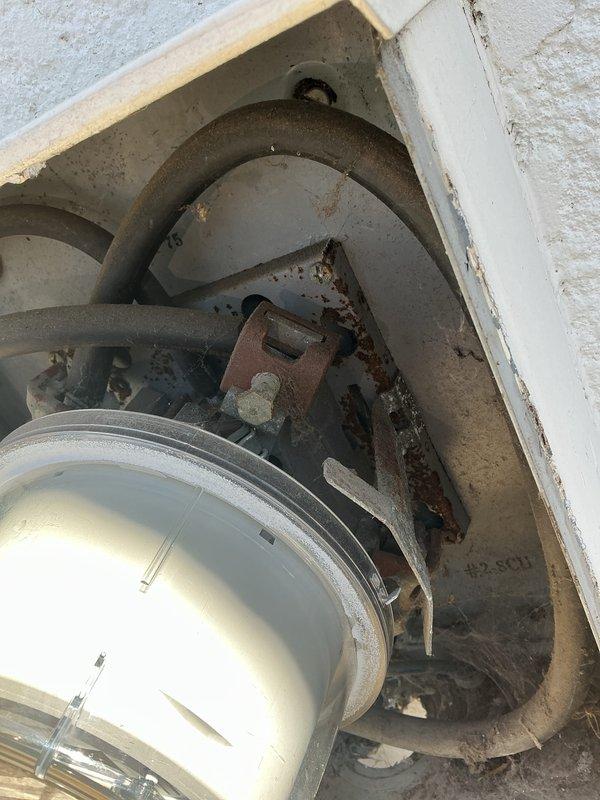 Conducted electrical inspection of HVAC system components, documenting significant rust and corrosion on metal brackets and mounting hardware. Observed improper wiring connections with accumulated dust and cobwebs, particularly around the #2.8CU marked area, indicating maintenance issues requiring attention.