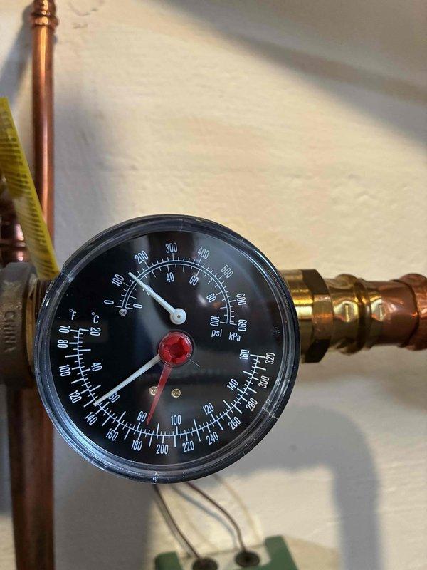 Performed routine heating maintenance inspection on boiler system. Examined pressure gauge on copper piping, confirming proper temperature and pressure readings within operational parameters. Inspected condensate drain assembly, noting aging in the translucent plastic fitting with mineral buildup and verifying proper drainage through the white flexible hose with secure clamp connection.