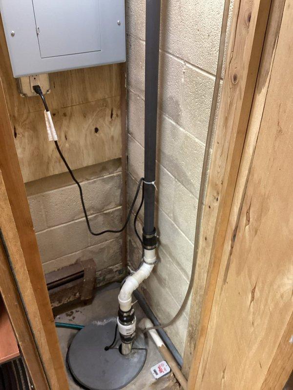 Conducted a comprehensive plumbing inspection of the basement utility area, examining the sump pump system with metal basin and PVC discharge piping. Also evaluated the water supply configuration featuring multiple copper pipes with blue valve handles and associated connections. All components appeared properly installed and functional with no immediate issues identified.