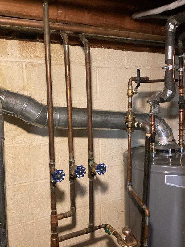 Conducted a comprehensive plumbing inspection of the basement utility area, examining the sump pump system with metal basin and PVC discharge piping. Also evaluated the water supply configuration featuring multiple copper pipes with blue valve handles and associated connections. All components appeared properly installed and functional with no immediate issues identified.
