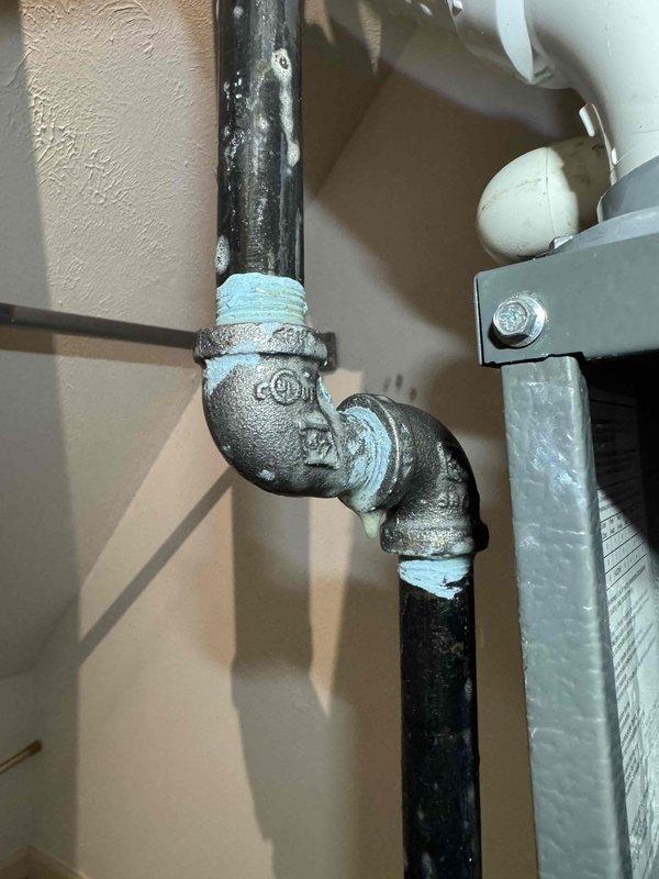 Responded to customer complaint of gas-like odor from furnace. Inspection revealed corrosion on gas pipe connections and fittings, particularly at the elbow joint. Documented oxidation and aging of cast iron pipes as well as condition of shut-off valve and PVC/metal pipe transitions in the utility area.