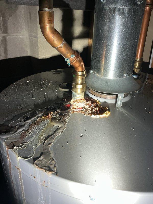 Conducted inspection of water heater exhibiting significant leakage from top surface. Observed extensive corrosion damage on upper portion of tank with visible moisture accumulation, compromised copper pipe connections showing greenish corrosion at joints, and mineral buildup around brass fittings. Documented evidence of advanced deterioration requiring replacement recommendation.