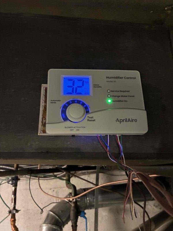 Successfully installed AprilAire Model 60 humidifier system with PVC drainage piping and clear tubing for proper water flow. Unit was calibrated, tested, and confirmed operational with humidistat displaying 32% relative humidity and green "Humidifier On" indicator illuminated.