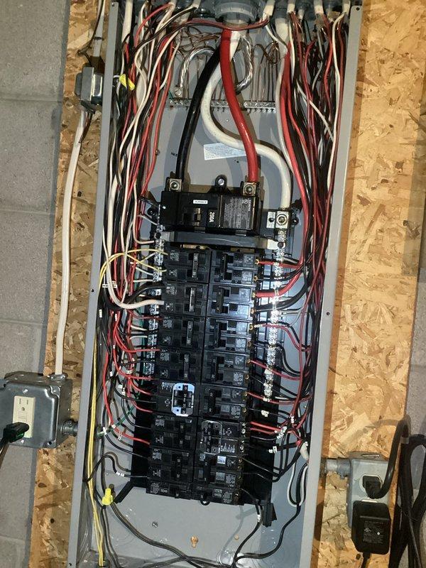 Conducted electrical panel inspection, documenting the main breaker panel with cover removed to examine circuit breaker configuration and wiring integrity. Observed proper wire routing with red, black, and white conductors appropriately organized, while also noting nearby plumbing infrastructure to ensure adequate clearances and no potential water hazards to electrical components.