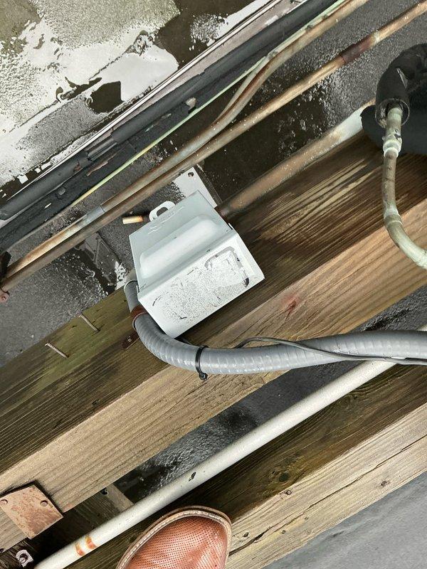 Conducted comprehensive assessment of rooftop heat pump unit requiring replacement, noting significant wear and water damage to the existing system. Observed deterioration of electrical connections including junction box mounted on wooden joists with visible moisture concerns. Documented conduit/flexible tubing condition and copper line positioning for proper replacement planning.