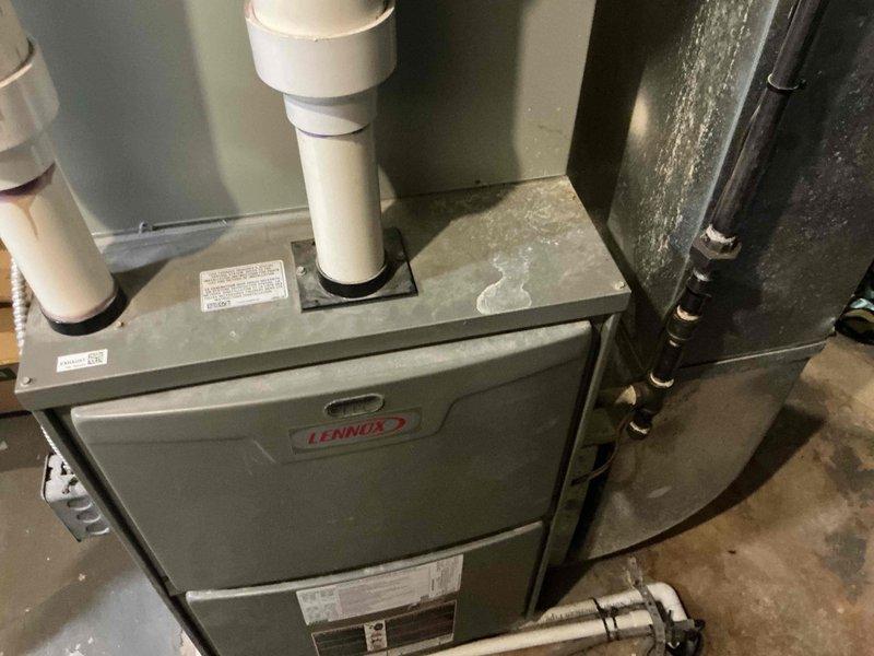 Conducted inspection of Lennox furnace system in utility area reporting "no heat" issue. Observed significant moisture accumulation on unit surface and documented existing installation including PVC intake/exhaust configuration. Provided customer with replacement options based on assessment of current system condition.