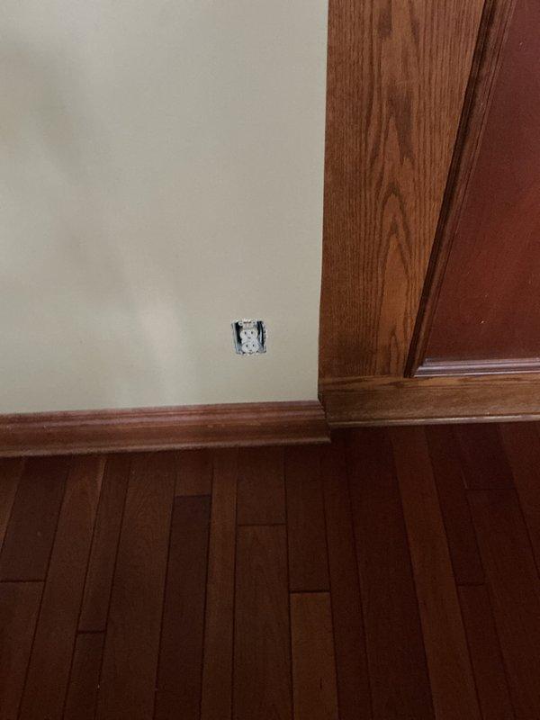 Conducted comprehensive electrical inspection, photographing and documenting an exposed wall outlet requiring installation completion and examining the circuit breaker panel which showed organized but crowded wiring with multiple red/white conductors and black cables entering from the top.