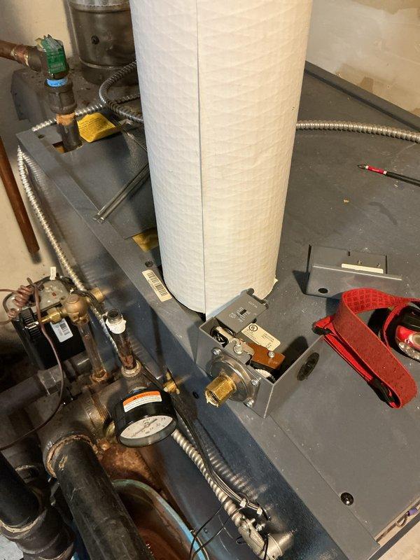 Performed scheduled boiler maintenance service on water heating system. Inspected aging copper piping showing oxidation at joints, checked pressure readings, and examined the blue cabinet housing with exposed wiring. Noted minor corrosion on metal components and previous water staining at unit base, but system remains functional after service.