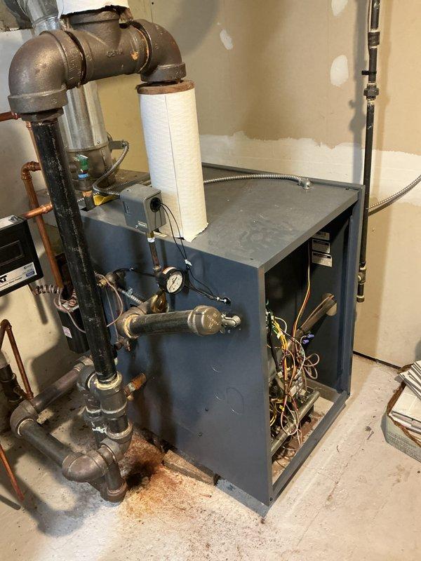 Performed scheduled boiler maintenance service on water heating system. Inspected aging copper piping showing oxidation at joints, checked pressure readings, and examined the blue cabinet housing with exposed wiring. Noted minor corrosion on metal components and previous water staining at unit base, but system remains functional after service.