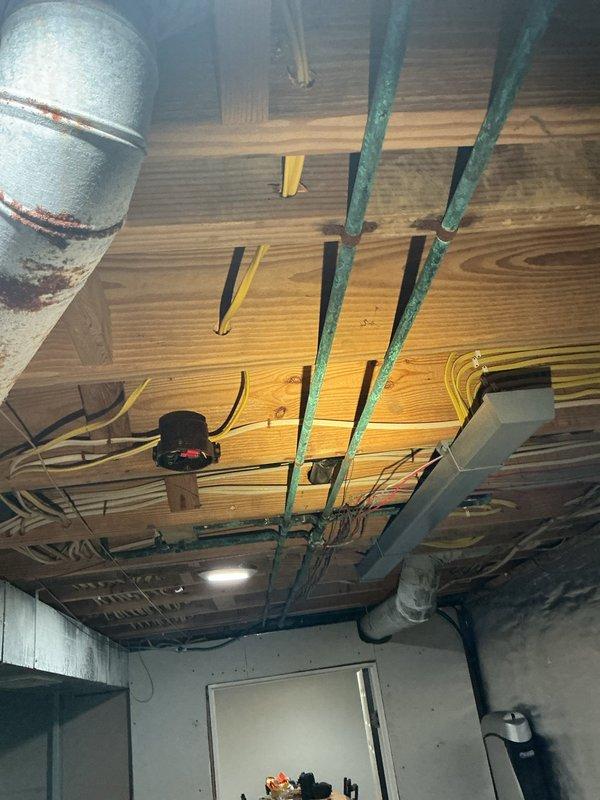 Conducted comprehensive plumbing inspection focusing on aging copper supply lines exhibiting significant verdigris and corrosion throughout the unfinished space. Documented condition of plumbing infrastructure including copper pipes mounted to wooden structural elements, adjacent PVC lines, and associated mounting hardware to assess system integrity and identify potential failure points.