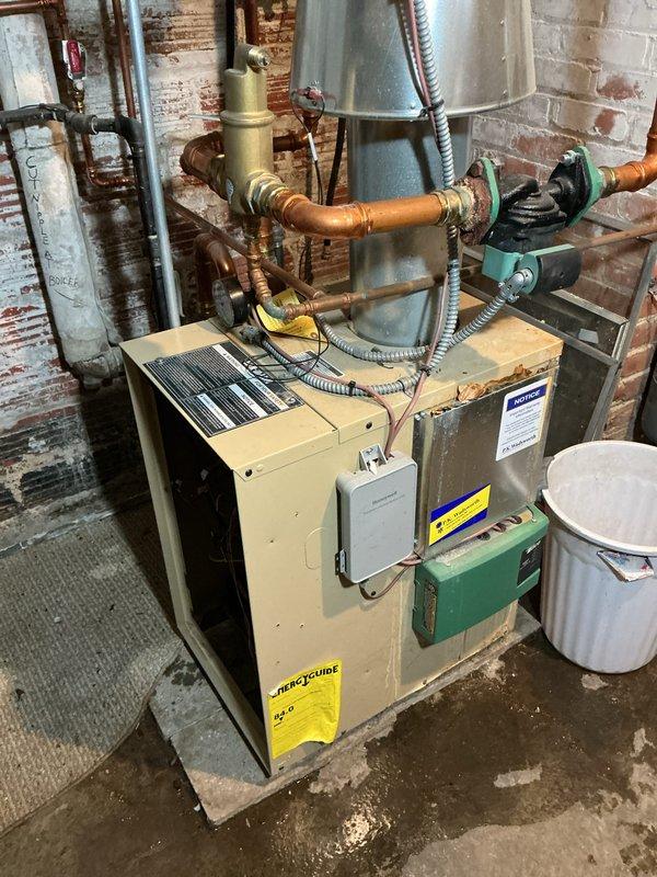 Performed scheduled maintenance on aging HVAC heating system located in basement utility area. Inspected and cleaned copper heat transfer components showing normal wear. System includes furnace unit with connected ductwork, flue piping, circulation pump assembly, and associated valves all functioning within acceptable parameters.