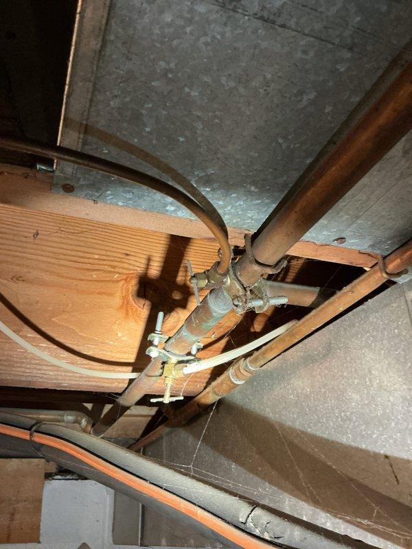 Conducted comprehensive plumbing inspection of residential property, focusing on exposed copper supply lines and gas connections in basement/utility area. Documented condition of piping system, noting normal oxidation on copper lines and examining brass T-fitting connections. Photographed structural installation through floor joists and utility connections including yellow flexible gas connector for documentation and future reference.