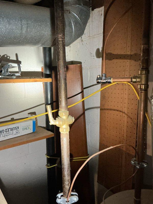 Conducted comprehensive plumbing inspection of residential property, focusing on exposed copper supply lines and gas connections in basement/utility area. Documented condition of piping system, noting normal oxidation on copper lines and examining brass T-fitting connections. Photographed structural installation through floor joists and utility connections including yellow flexible gas connector for documentation and future reference.