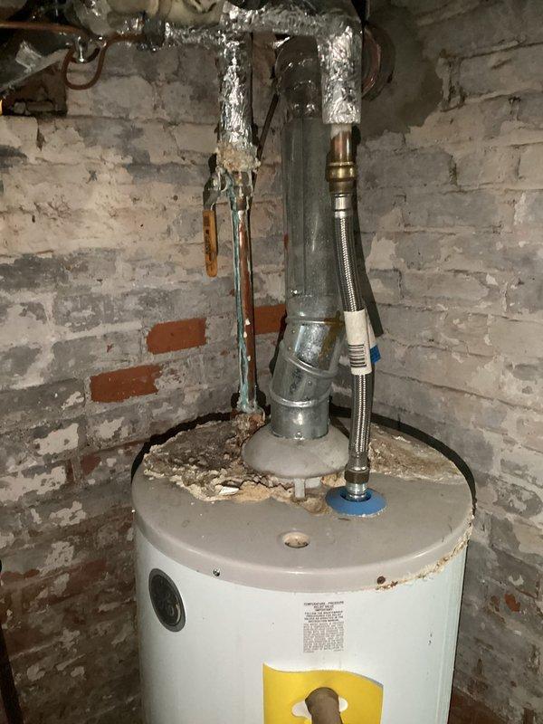 Completed comprehensive plumbing inspection of residential water heater system and documented current condition with photographic evidence. Water heater exhibited visible signs of aging including rust corrosion around upper rim and pressure relief valve assembly, peeling paint on surrounding brick wall, and sediment accumulation at base, with all supply lines, copper piping, reflective insulation wrapping, and flexible braided connections visually assessed for immediate safety concerns.