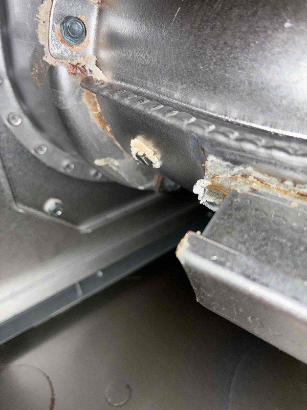 # HVAC Service Report - No Heat Emergency Call

Responded to emergency no heat call for gas furnace system located in attic with partial heating failure affecting guest bedrooms. Customer reported unit would power on and begin cycling but shut down shortly after, with temporary operation achieved only through manual adjustment of inducer motor.

Upon inspection, found aging furnace system with significant deterioration of blower housing and associated components. Visual examination revealed extensive rust and corrosion along blower assembly seams and edges, with heavy orange-brown oxidation present on circular housing components. White crystalline deposits and mineral buildup observed near corroded areas, indicating prolonged moisture exposure. Metal surfaces throughout unit showed advanced aging with dusty accumulation and multiple areas of deterioration.

Primary issue identified as failed inducer motor assembly preventing proper combustion air management and causing safety lockout d