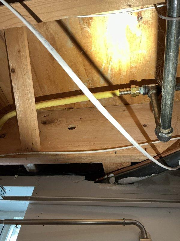 Responded to report of gas leak originating from beneath kitchen area in basement. Upon inspection, accessed crawl space and examined exposed gas piping system running through ceiling joists. Located copper gas line with brass fittings and connections running horizontally through the space. Conducted visual inspection of all accessible gas line sections, joints, and fittings for signs of leakage or damage. Documented existing piping configuration including routing near PVC plumbing lines and HVAC ductwork. Further pressure testing recommended to confirm leak location and ensure system integrity before proceeding with repairs.