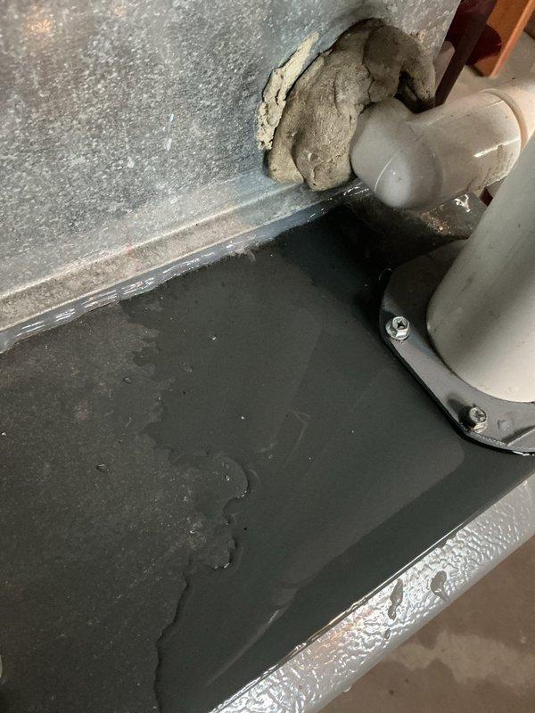 Responded to customer report of furnace water leak in basement mechanical room. Upon inspection, examined gray metal furnace unit with white PVC condensate drainage piping system running vertically and horizontally with multiple elbow joints. Inspected all condensate drain connections, pipe penetrations through wall surfaces, and drain line routing. Photographed installation showing PVC drain line secured with metal straps at wall penetration point, noting patching material and sealing compound around pipe opening. Verified proper drainage slope and checked for blockages in condensate system. Documented equipment layout including furnace, water heater, and dehumidifier unit to assess potential leak sources and drainage pathways.