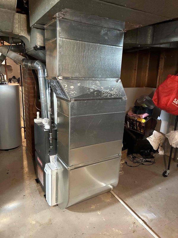 Completed installation of new Goodman 80% efficiency furnace in residential basement mechanical room. Unit installed on concrete pad with proper clearances, connected to existing ductwork system via galvanized metal plenum and distribution network, and tested for proper operation and airflow.