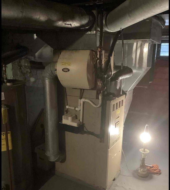 Conducted comprehensive evaluation of existing HVAC system for replacement estimate. Assessed outdoor condensing unit showing significant weathering, surface deterioration, and debris accumulation on exterior pad. Documented indoor furnace assembly with integrated humidifier system and associated ductwork configuration in basement mechanical room. Photographed current equipment conditions, refrigerant line routing, electrical connections, and ductwork layout to provide replacement options and system specifications.