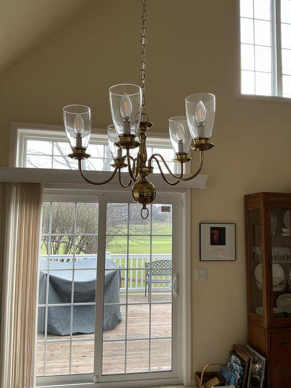 Installed a five-arm brass chandelier with candle-style bulbs and clear glass hurricane shades in dining area at ceiling height of 15-18 feet. Verified proper electrical connections, tested dimmer switch functionality, and confirmed all bulbs illuminated correctly upon completion.
