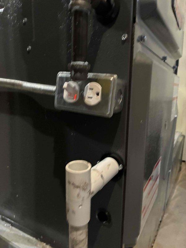 Completed installation of 96% efficiency furnace with scrubber system, including proper venting with white PVC piping routed through existing wall cavity with fiberglass insulation for weatherization. Electrical outlet box with GFCI protection mounted to unit panel, with coordination noted for licensed electrician to complete surge protector installation at later time.