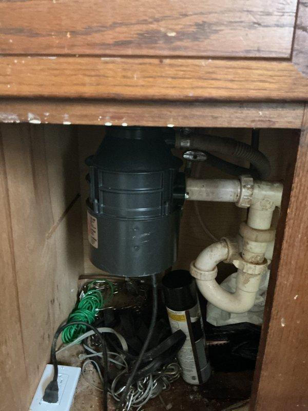 Performed comprehensive plumbing inspection of kitchen sink and drainage system. Diagnosed completely clogged garbage disposal unit and standing water issue in left basin. Documented under-sink plumbing configuration including disposal unit, PVC trap assembly, and cabinet condition for recommended repairs.