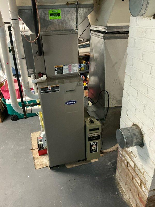 Conducted on-site assessment of existing Carrier furnace system in basement mechanical room to provide replacement options. Evaluated current equipment configuration, including ductwork connections, venting system with white PVC piping, and overall HVAC infrastructure layout. Documented existing furnace installation on wooden support planks, metallic ductwork distribution system, and humidifier components for replacement planning purposes.