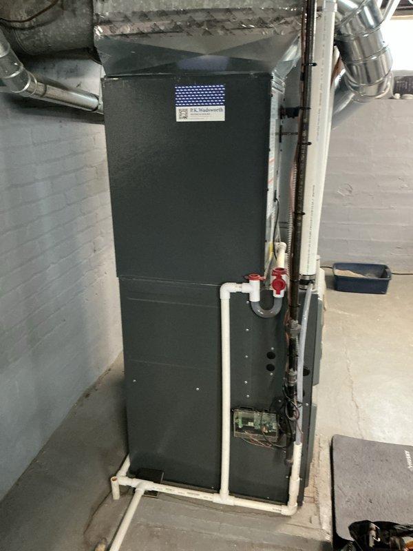 Completed routine heating maintenance on residential air handler unit located in basement mechanical room. Performed comprehensive system inspection including verification of all electrical connections, ductwork integrity, and condensate drainage system. Confirmed Aprilaire humidity control device operating properly with digital display reading 56% and all wiring connections secure. Inspected PVC condensate piping with red valve fitting, verified proper drainage flow and no blockages present. Checked air handler cabinet condition, mounting stability on wooden platform base, and all ductwork connections at top and side of unit. System tested and operating within normal parameters with no issues identified requiring immediate attention.