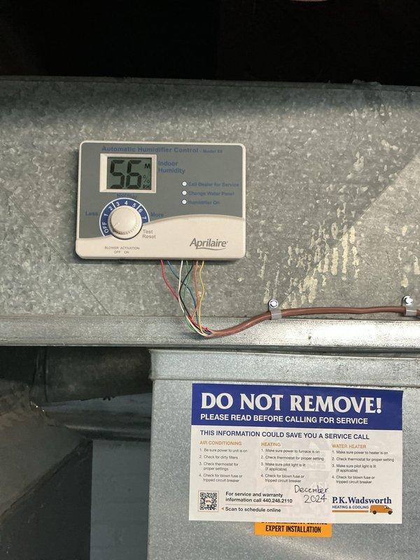 Completed routine heating maintenance on residential air handler unit located in basement mechanical room. Performed comprehensive system inspection including verification of all electrical connections, ductwork integrity, and condensate drainage system. Confirmed Aprilaire humidity control device operating properly with digital display reading 56% and all wiring connections secure. Inspected PVC condensate piping with red valve fitting, verified proper drainage flow and no blockages present. Checked air handler cabinet condition, mounting stability on wooden platform base, and all ductwork connections at top and side of unit. System tested and operating within normal parameters with no issues identified requiring immediate attention.