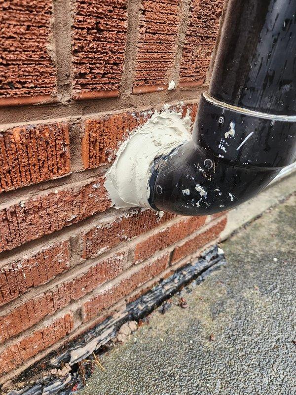 Eliminated prohibited saddle valve connection on humidifier water supply line and replaced with code-compliant plumbing installation. Removed non-approved joints and fittings, ensuring all connections meet current mechanical code requirements. Documented all modifications with photographs showing exterior drainage components and foundation area where work was performed.