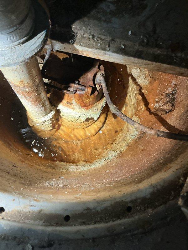Responded to service call for non-operational sump pump system requiring replacement. Upon inspection, found existing sump pump basin and components exhibiting severe corrosion, rust accumulation, and standing water with rust-colored sediment. The interior of the sump pit displayed extensive deterioration with compromised metal surfaces, corroded piping connections, and degraded mechanical components. Documented existing conditions showing failed pump assembly with heavily oxidized basin, deteriorated discharge piping with white PVC connections, and significant rust buildup throughout the system indicating prolonged exposure to moisture and lack of functionality.