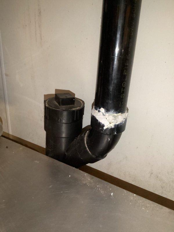 Conducted plumbing estimate for basement piping replacement. Assessed existing black PVC drainage system with 90-degree elbow configuration mounted against concrete block wall. Documented current pipe condition, including visible sealant application at connection points and overall system layout. Photographed installation to provide comprehensive evaluation for required piping replacement work in utility area.