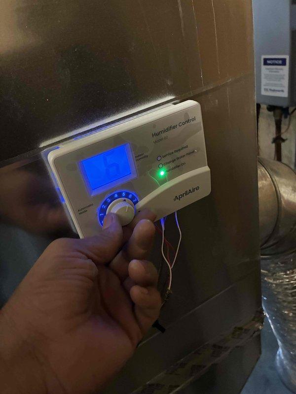 Installed a fan-powered humidifier system with Aprilaire Model 60 wall-mounted digital control unit. The control panel features an LCD display, numbered rotary dial settings, and automatic/manual/test mode functionality, mounted and wired to integrate with the existing HVAC air handler for whole-home humidity management.