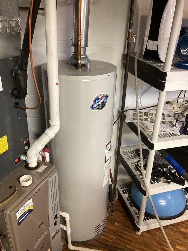 Performed courtesy inspection of residential water heating system. Documented 2008 conventional tank water heater with active leak originating from tank or valve assembly. Photographed existing equipment configuration including copper supply lines, shut-off valves, and connections to evaluate replacement options. Discussed tankless water heater alternatives with homeowner as potential upgrade solution.