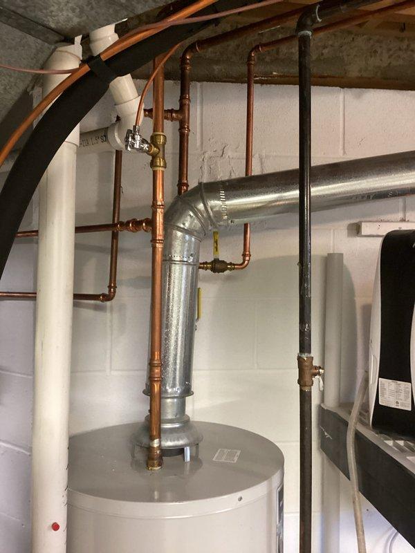 Performed courtesy inspection of residential water heating system. Documented 2008 conventional tank water heater with active leak originating from tank or valve assembly. Photographed existing equipment configuration including copper supply lines, shut-off valves, and connections to evaluate replacement options. Discussed tankless water heater alternatives with homeowner as potential upgrade solution.