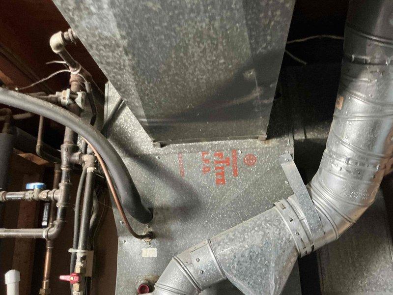 Completed full system assessment for replacement of 30-year-old HVAC system with non-functional furnace and air conditioning unit at end of service life. Documented existing indoor equipment showing significant condensation on galvanized plenum and ductwork, along with refrigerant lines and associated mechanical connections in basement installation. Evaluated outdoor condenser unit mounted on concrete pad against exterior fence, noting refrigerant line routing and overall system configuration to provide comprehensive replacement estimate for complete heating and cooling system.