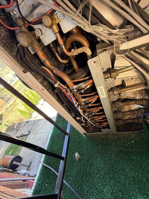 Responded to service call for Samsung mini-split system with reported refrigerant leak and no cooling. Upon inspection, discovered significant corrosion on outdoor unit copper piping and heat exchanger assembly, with visible oxidation on U-bend configuration and brass fittings. Documented condition of wall-mounted indoor evaporator unit and corroded outdoor condenser coil assembly mounted under elevated structure. Photographed leak source areas and provided assessment of system condition for repair recommendations.
