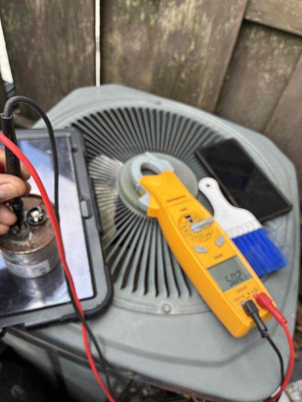 Completed comprehensive maintenance service on dual HVAC systems including heating and cooling equipment. Performed diagnostic testing on outdoor condenser unit with digital multimeter to evaluate capacitor performance and verify proper electrical function. Inspected internal fan assembly and motor components with top grille removed for thorough access. 

Identified severely corroded and deteriorated brass terminal connector showing evidence of overheating and electrical arcing damage with significant oxidation buildup. Terminal exhibited green and brown corrosion with melted metal around edges indicating previous thermal stress. Assessed electrical connections including red, yellow, blue, and brown wire terminations on black housing assembly. Documented excessive dirt, grime, and debris accumulation throughout electrical components affecting system reliability and performance. 

Conducted full system evaluation per maintenance protocol to ensure safe and efficient operation of both he